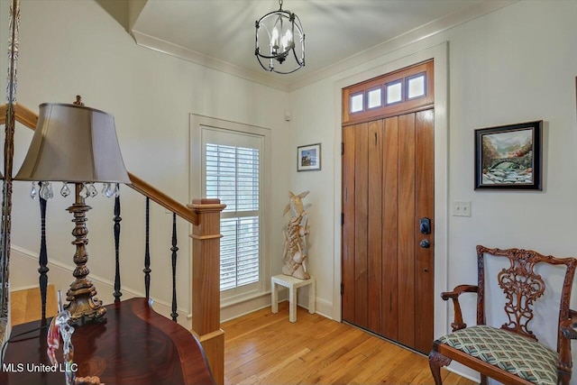 entrance foyer with a notable chandelier, light hardwood / wood-style flooring, ornamental molding, and plenty of natural light