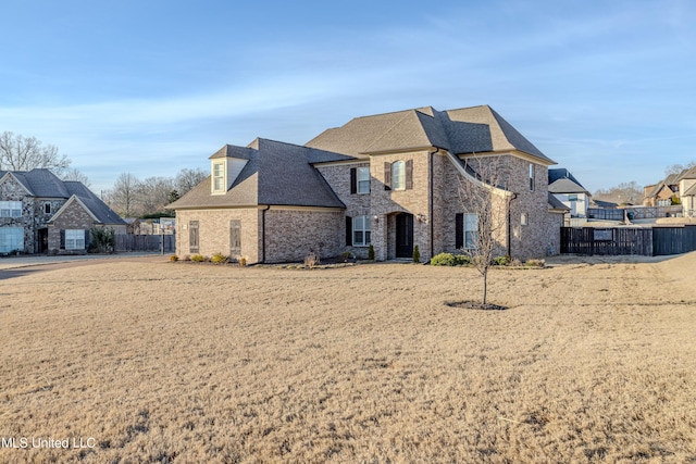 french provincial home featuring brick siding, roof with shingles, and fence