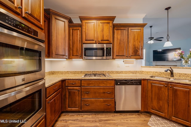 kitchen with light wood-style flooring, brown cabinets, light stone countertops, stainless steel appliances, and a sink