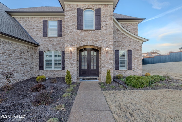 entrance to property with brick siding, a shingled roof, fence, and french doors