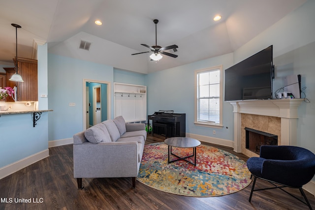 living room featuring dark wood-type flooring, visible vents, baseboards, vaulted ceiling, and a tiled fireplace