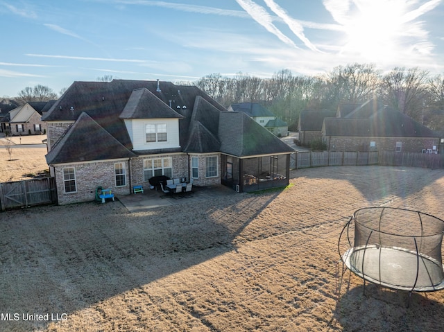 rear view of house with stone siding, a trampoline, and fence