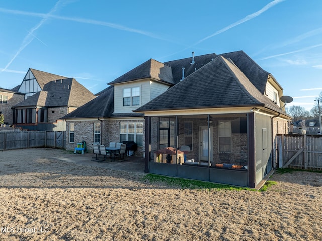 back of property with brick siding, a patio, a shingled roof, a sunroom, and a fenced backyard