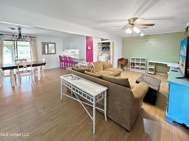 living room with independent washer and dryer, light hardwood / wood-style floors, and ceiling fan with notable chandelier