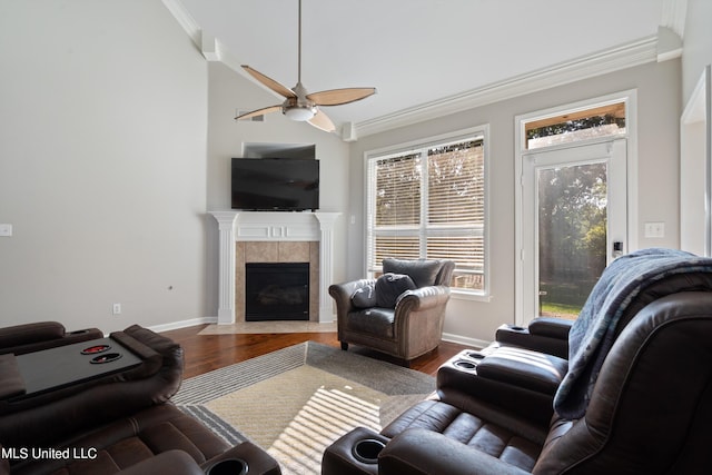 living room featuring crown molding, a tiled fireplace, wood-type flooring, and ceiling fan