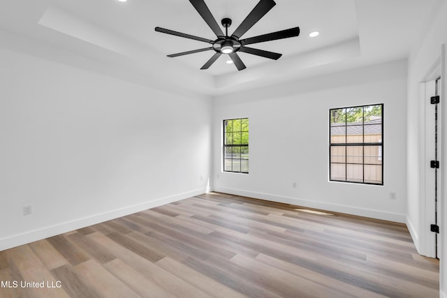 spare room with recessed lighting, ceiling fan, baseboards, light wood-type flooring, and a raised ceiling