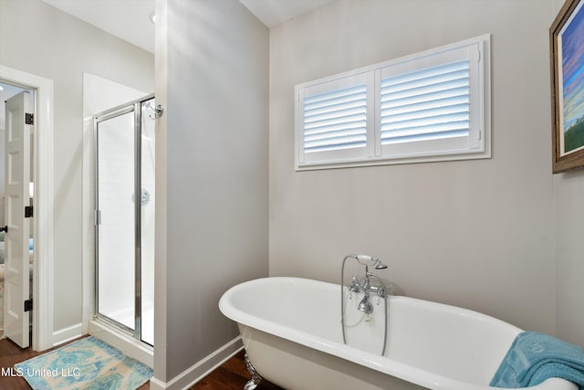 bathroom with a shower stall, a freestanding bath, baseboards, and wood finished floors
