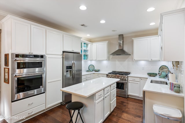 kitchen featuring dark wood-style flooring, a sink, stainless steel appliances, wall chimney exhaust hood, and ornamental molding