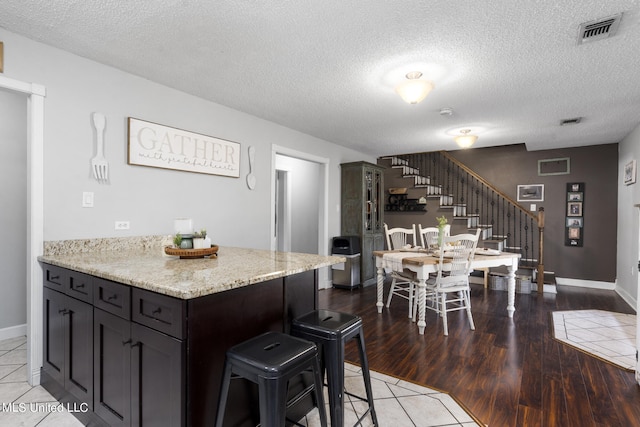 kitchen featuring light stone countertops, a textured ceiling, a kitchen breakfast bar, dark brown cabinetry, and dark wood-type flooring