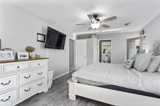 bedroom featuring ensuite bath, a textured ceiling, dark hardwood / wood-style floors, and ceiling fan