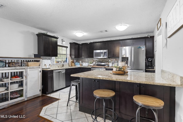 kitchen with a breakfast bar area, appliances with stainless steel finishes, a textured ceiling, light hardwood / wood-style flooring, and light stone counters