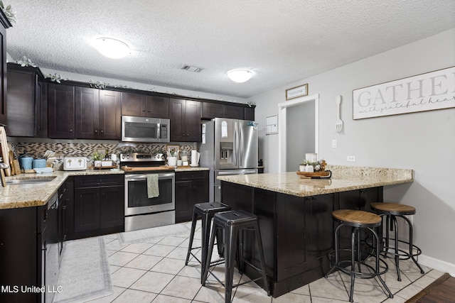 kitchen featuring appliances with stainless steel finishes, kitchen peninsula, a textured ceiling, and a breakfast bar area