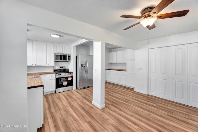 kitchen featuring light wood finished floors, appliances with stainless steel finishes, a ceiling fan, white cabinets, and baseboards