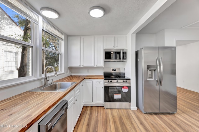 kitchen featuring stainless steel appliances, butcher block counters, white cabinetry, and a sink