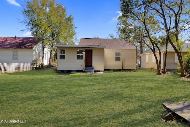 rear view of property featuring entry steps, a yard, a shingled roof, and fence