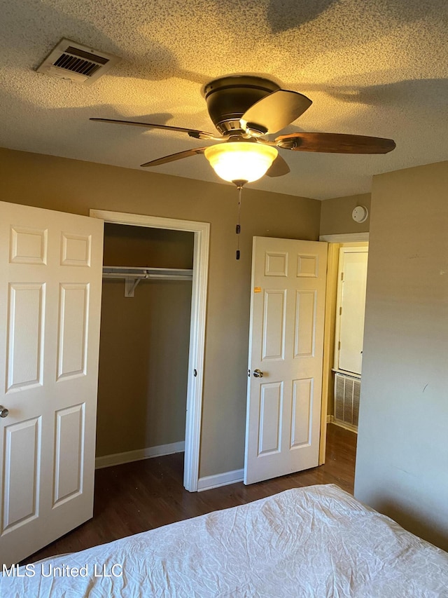 unfurnished bedroom with dark hardwood / wood-style flooring, a textured ceiling, ceiling fan, and a closet