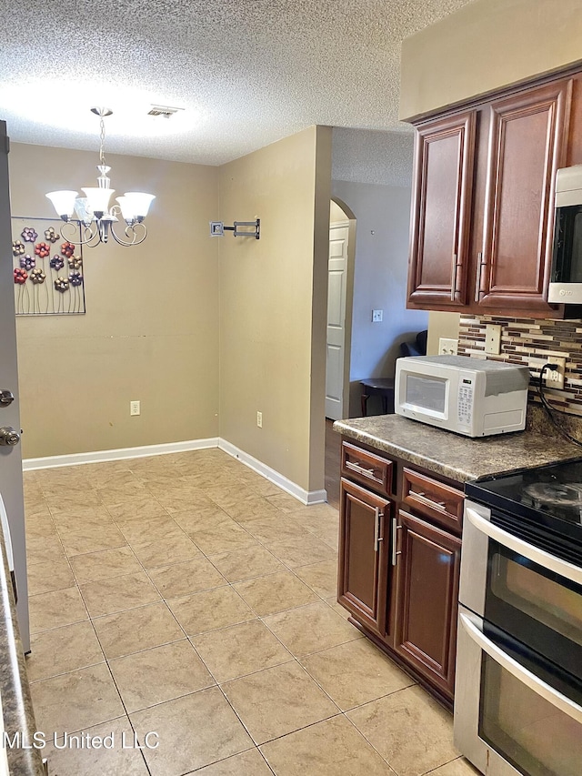 kitchen featuring appliances with stainless steel finishes, light tile patterned floors, a notable chandelier, decorative light fixtures, and backsplash