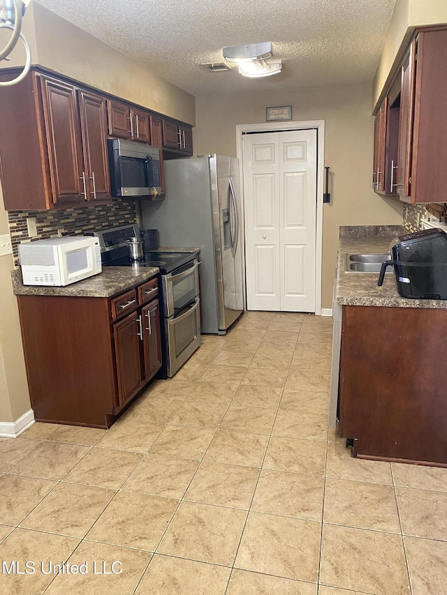 kitchen featuring light tile patterned flooring, a textured ceiling, and appliances with stainless steel finishes