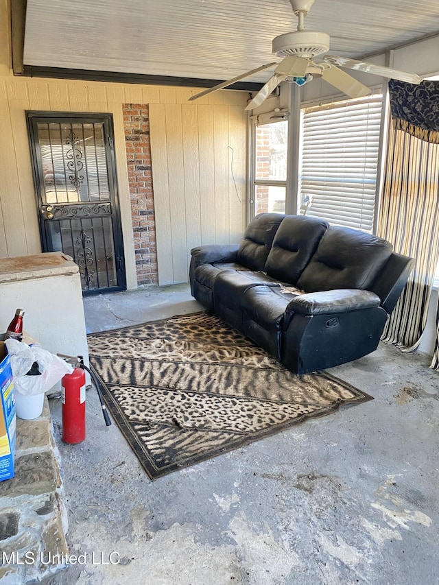 living room with ceiling fan, concrete floors, and wood walls