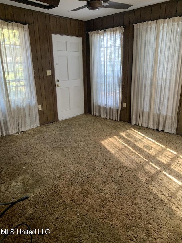 interior space with ceiling fan and wooden walls