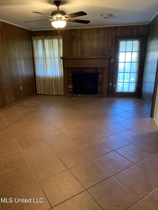 unfurnished living room featuring crown molding, wooden walls, ceiling fan, light tile patterned floors, and a fireplace