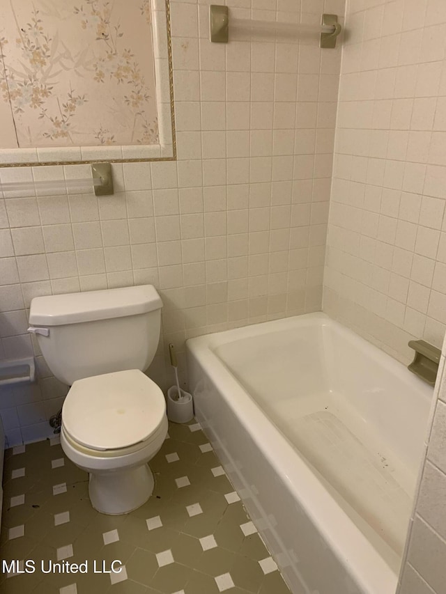 bathroom featuring a bath, tile walls, and toilet