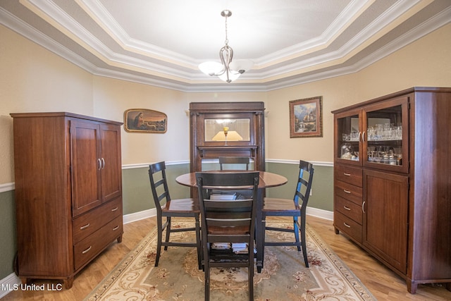 dining area featuring light wood-type flooring, a tray ceiling, an inviting chandelier, and ornamental molding