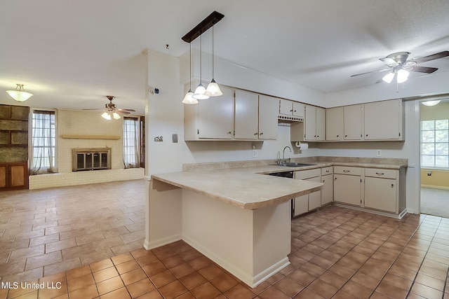 kitchen with sink, kitchen peninsula, a brick fireplace, ceiling fan, and decorative light fixtures