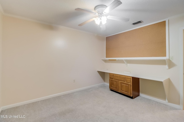 unfurnished office featuring built in desk, ornamental molding, light carpet, and ceiling fan