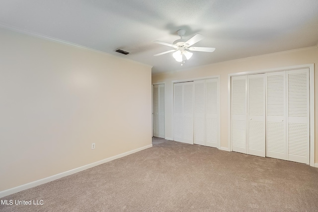 unfurnished bedroom with ceiling fan, light carpet, crown molding, and two closets