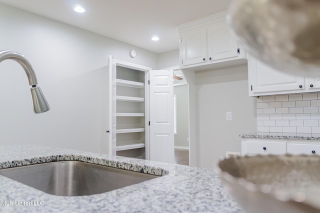 kitchen with a sink, light stone countertops, white cabinets, tasteful backsplash, and recessed lighting