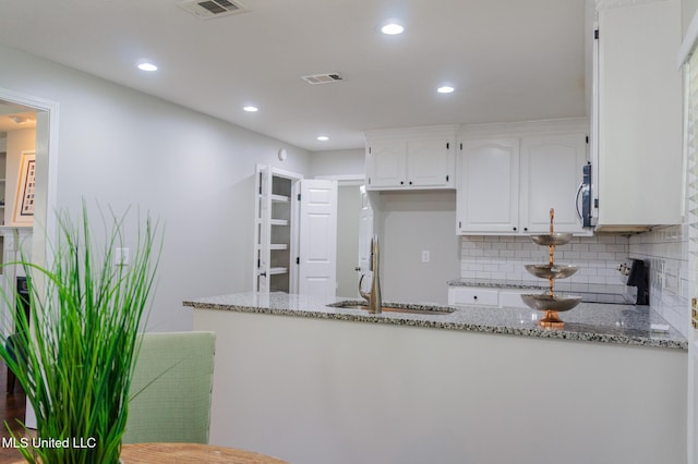 kitchen with a sink, light stone counters, white cabinets, backsplash, and recessed lighting