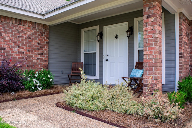 view of exterior entry featuring brick siding and a shingled roof
