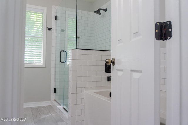 full bath featuring a shower stall, healthy amount of natural light, baseboards, and a garden tub