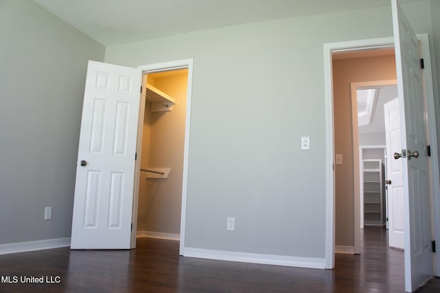 unfurnished bedroom featuring a walk in closet, dark wood finished floors, baseboards, and a closet