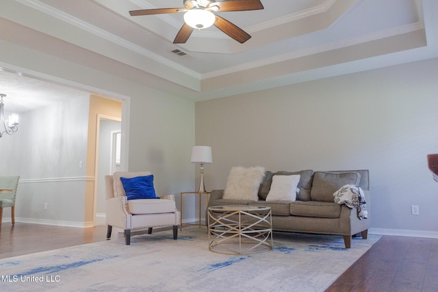 living room featuring wood finished floors, ornamental molding, a chandelier, baseboards, and a tray ceiling