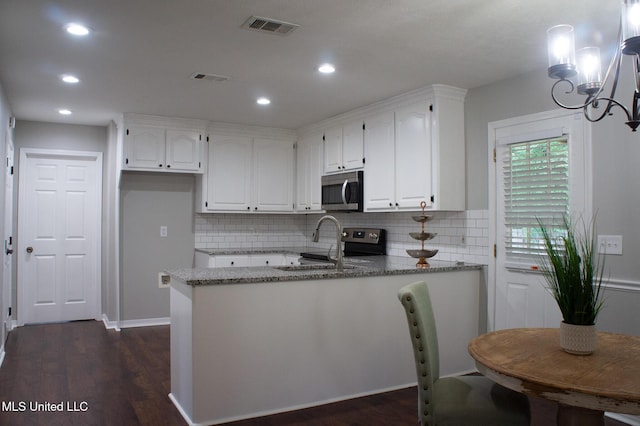 kitchen with stainless steel appliances, a sink, white cabinetry, a peninsula, and dark wood finished floors