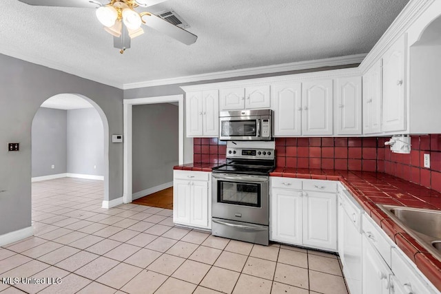 1320 Sally Dr, Picayune, MS 39466 - kitchen featuring appliances with stainless steel finishes, tile counters, arched walkways, a textured ceiling, and white cabinets