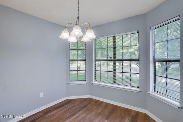 unfurnished dining area with dark wood finished floors, baseboards, and a notable chandelier
