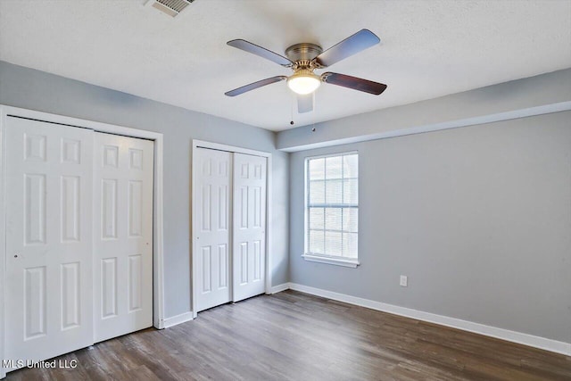 unfurnished bedroom with a ceiling fan, two closets, visible vents, dark wood-style flooring, and baseboards