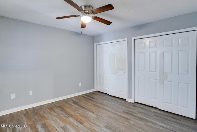 unfurnished bedroom with ceiling fan, baseboards, multiple closets, and wood finished floors