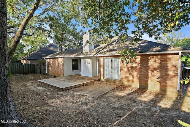 rear view of house featuring brick siding, a chimney, fence, and a wooden deck