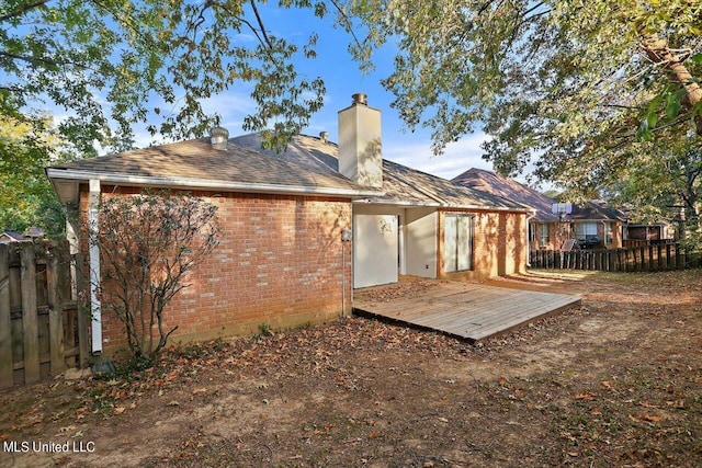 rear view of house featuring a chimney, a wooden deck, brick siding, and fence