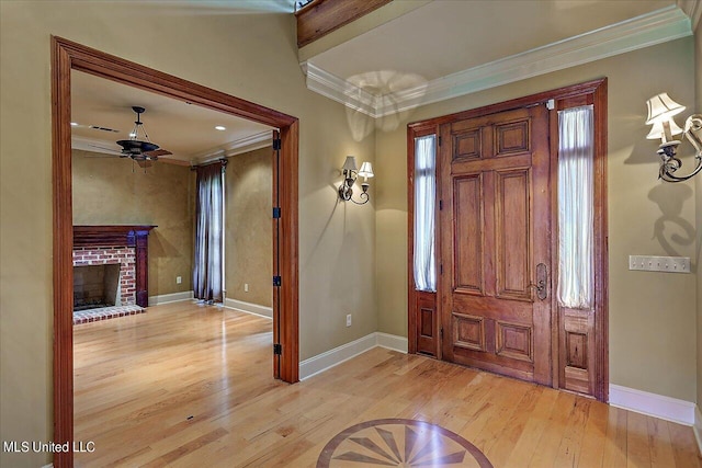 entryway with light wood-type flooring, a brick fireplace, crown molding, and ceiling fan