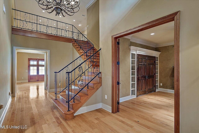 foyer entrance featuring a high ceiling, hardwood / wood-style floors, ornamental molding, and a notable chandelier