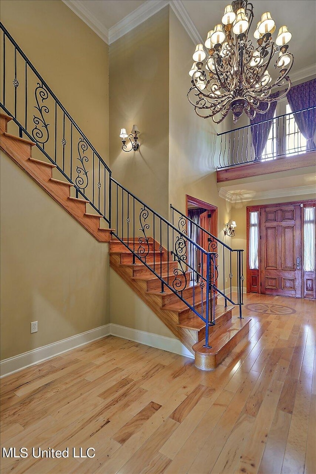 entryway with a towering ceiling, ornamental molding, and light hardwood / wood-style flooring