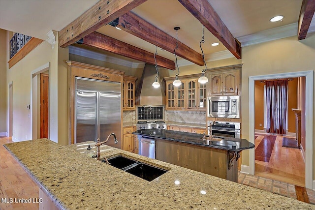 kitchen with decorative backsplash, sink, built in appliances, beamed ceiling, and an island with sink