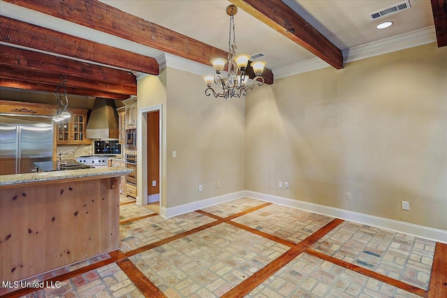 kitchen featuring a notable chandelier, wall chimney range hood, pendant lighting, decorative backsplash, and built in appliances