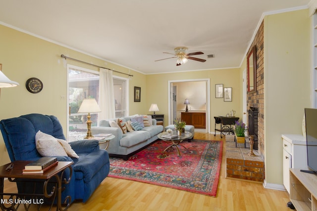 living room with a brick fireplace, crown molding, light hardwood / wood-style floors, and ceiling fan