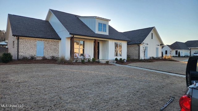 modern farmhouse style home with brick siding, a porch, board and batten siding, and roof with shingles